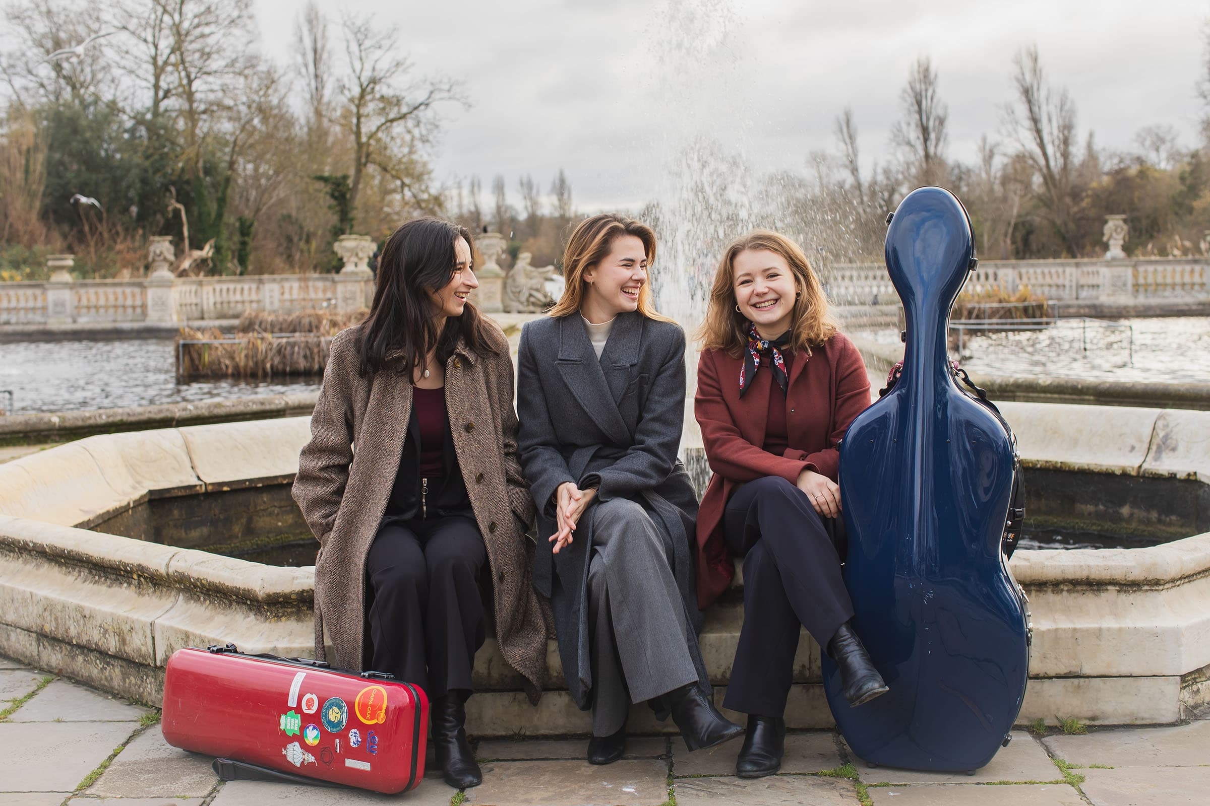 Aida Piano Trio seated outdoors by a fountain